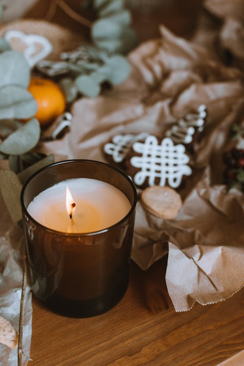 Lighted candle on a table beside cookies and fresh orange slices, creating a cozy seasonal ambiance with warm scents for the home