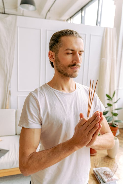 Man meditating while burning incense sticks to create a calming aromatherapy atmosphere as part of a daily self-care ritual