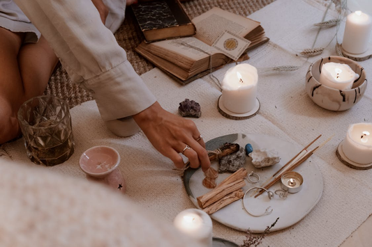 Woman’s hand reaching toward a plate of wax candles surrounded by incense sticks, creating a calming spa-like aromatherapy setup at home